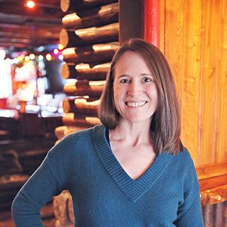 The author standing in front of a log cabin with soft, warm lighting