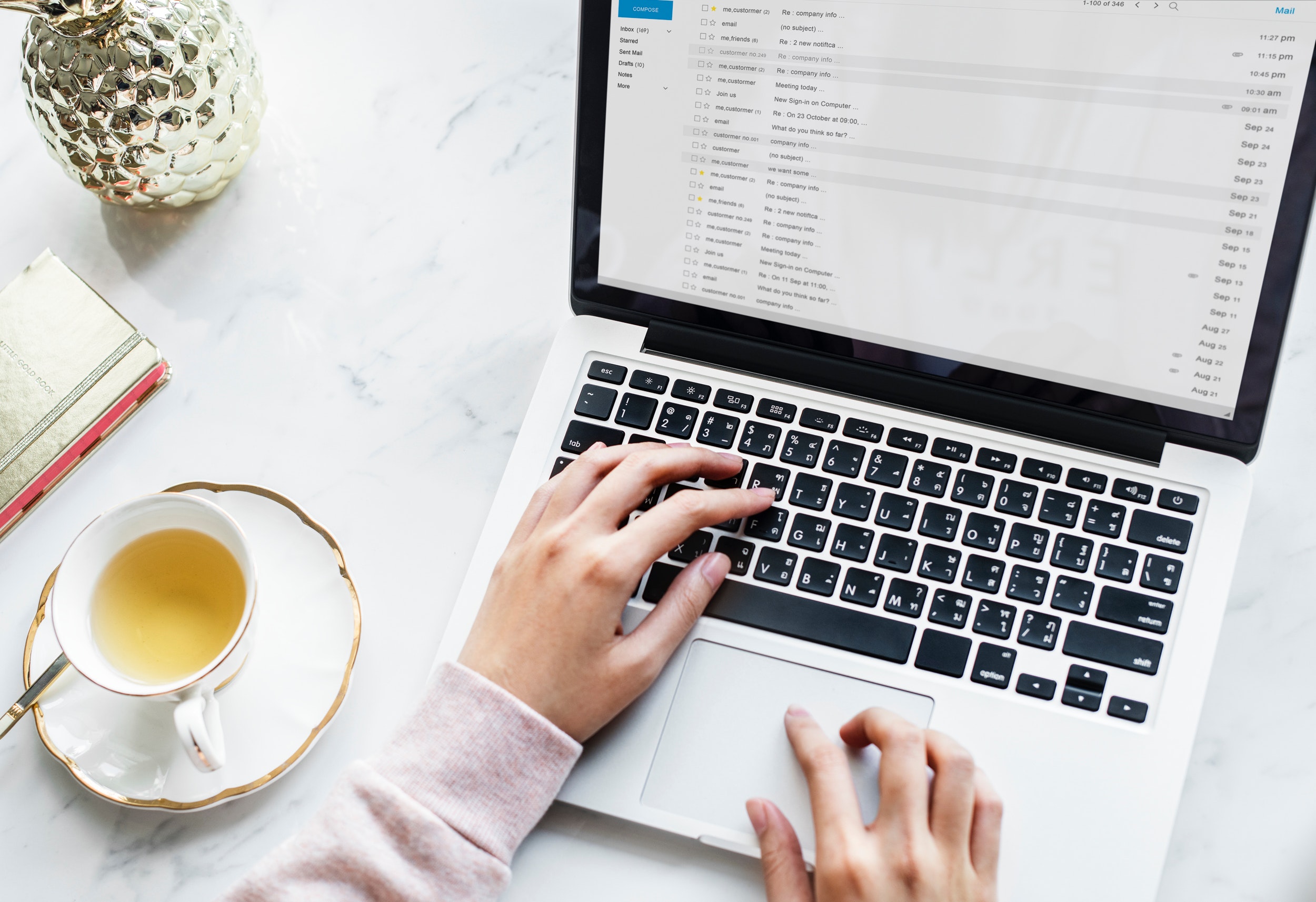 Closeup of hands typing on a laptop next to a cup of tea