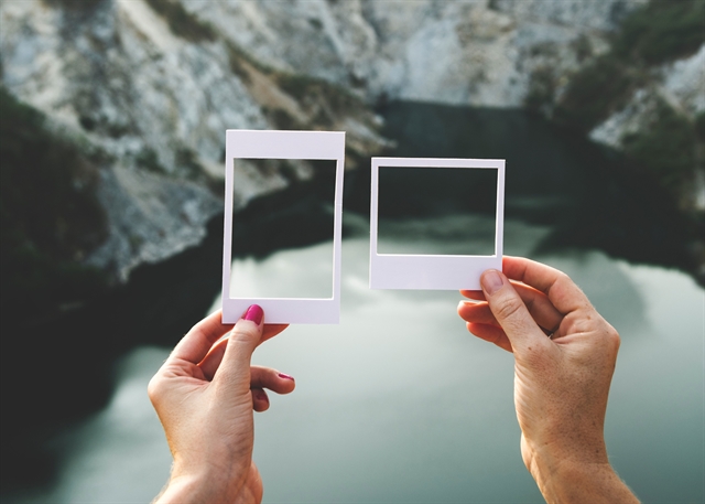 Hands holding paper frames in front of rocks and water