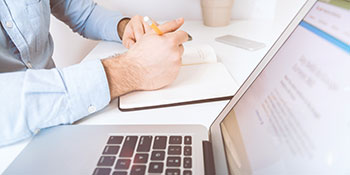 Man at a desk working on his laptop and writing notes Man at a desk working on his laptop and writing notes