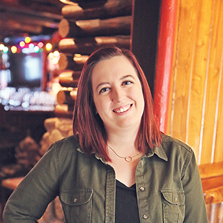 Woman standing in front of a log cabin with soft, warm lighting